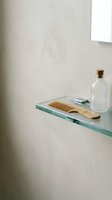 Minimalist bathroom shelf displaying wooden comb, white bottle with cork stopper, and folded towel on glass ledge against neutral wall. Spa and wellness styling.