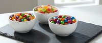 Colorful candy assortment in white bowls on slate board, featuring rainbow jellybeans and mixed sweets for party treats and confectionery displays.
