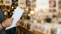 Person holding blank white paper in retail store environment with blurred merchandise and warm lighting in background.