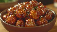Glazed Asian meatballs garnished with sesame seeds and fresh chopped herbs served in brown ceramic bowl, appetizing close up shot of traditional cuisine.