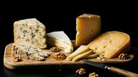 Gourmet cheese selection with blue cheese, aged cheddar and soft varieties arranged on wooden board with walnuts and knife for culinary presentations.