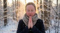 Young Caucasian woman meditating with prayer hands in snowy winter forest at golden hour sunrise, peaceful mindfulness and spiritual wellness concept.