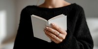 Person in black sweater holding open blank white book with natural light creating soft shadows, perfect for education or reading concepts.
