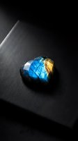 Polished labradorite gemstone with brilliant blue and golden flash on dark surface showcasing natural iridescent colors and mineral crystal formation.