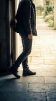 Man in casual dark clothing leaning against doorway on stone patio with warm natural lighting and garden background for lifestyle concepts.
