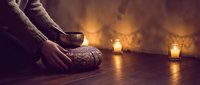 Woman in cozy knit sweater and socks holding warm tea cup in candlelit room creating peaceful hygge atmosphere for relaxation and comfort.