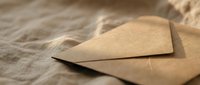 Vintage kraft paper envelope on rustic burlap fabric texture background for correspondence, wedding invitations and stationery design projects.