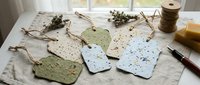 Handmade seed paper gift tags with embedded wildflower and herb seeds in natural colors, arranged on linen with twine and dried botanicals for eco-friendly crafting and sustainable packaging.