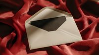 Open white envelope with black card on luxurious red velvet fabric, creating elegant contrast for wedding invitations or formal announcements.
