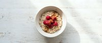 Healthy oatmeal breakfast bowl topped with fresh raspberries served in white ceramic dish on rustic wooden table background for morning meal nutrition.