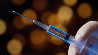 Medical professional holding syringe with vaccine or medication against warm bokeh background for healthcare and immunization concepts.