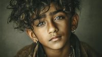 Young mixed-race boy with curly hair and piercing eyes in warm lighting portrait for emotional storytelling and diverse representation projects.