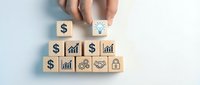 Hand placing lightbulb idea block above wooden cubes with dollar signs and business growth charts for financial planning and investment strategy concepts.