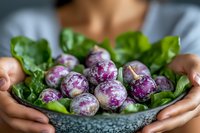 Fresh purple and white marbled turnips on green leaves held in gray stone bowl by female hands. Close up view of organic farm vegetables for healthy eating.