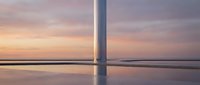 Minimalist wind turbine base reflected in still water at sunset with purple and golden sky tones, suitable for renewable energy and sustainability concepts.