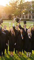 Diverse group of happy graduates in caps and gowns celebrating commencement ceremony on university campus, throwing mortarboards in air with diplomas.