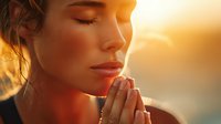 Young Caucasian woman with closed eyes praying at sunset, golden light illuminating her peaceful face as she holds hands together in meditation.