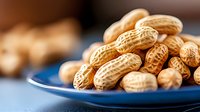 Fresh roasted peanuts in shell on blue ceramic plate, selective focus with natural lighting and blurred background, macro food photography.