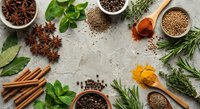 Aromatic spices and herbs arranged on rustic concrete surface with star anise, cinnamon sticks, peppercorns, turmeric, coriander seeds and fresh herbs for cooking.