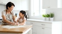 Adult woman of East Asian descent and young girl of East Asian descent baking together at kitchen counter, kneading dough, family bonding activity.