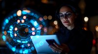 Young Asian businesswoman using digital tablet with futuristic holographic interface display in modern office environment at night.