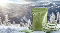 Green cosmetic package with fresh aloe vera leaves on snowy mountain background. Natural organic skincare product in winter landscape with sunlight and pine trees.
