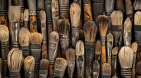 Collection of aged artist paintbrushes with wooden handles and natural bristles arranged in rows showing texture and wear from years of creative use.