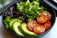 Fresh healthy salad bowl with sliced avocado, cherry tomatoes and mixed greens on dark plate. Nutritious vegetarian meal for clean eating and wellness lifestyle.