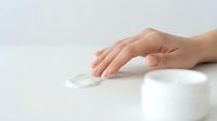 Close-up of a woman's hand applying white moisturizing cream from a jar, demonstrating skincare routine and cosmetic product usage for beauty and wellness.
