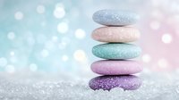 Balanced pastel zen stones stack on sparkly bokeh background in soft pink and mint tones, creating serene spa atmosphere. Wellness and meditation concept.