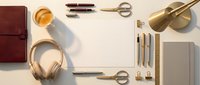 Elegant flat lay workspace with gold headphones, leather notebook, brass lamp and stationery items arranged on white background for modern office design.