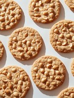 Fresh baked peanut butter cookies arranged in rows on white background, showing crispy texture and crunchy nuts pattern, for food photography and menu design.