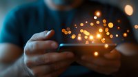 Person holding smartphone in dark with glowing magical light effects and bokeh emerging from screen, creating atmospheric mobile technology concept.