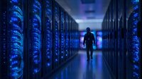 Silhouette of technician walking through modern data center corridor with rows of illuminated server racks glowing blue in high-tech facility.