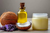 Natural coconut oil, fresh coconut, glass bottle with essential oil and lavender flowers on wooden surface against gray background. Organic skincare concept.