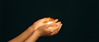 Hands cupped together holding glowing light orb against dark background, symbolizing hope, care, energy, and protection for wellness and spirituality concepts.