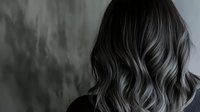 Luxurious dark wavy hair with silver grey highlights styled in loose curls against moody background, professional salon result showing modern balayage technique.