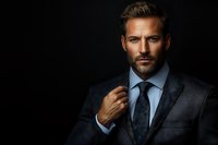 Confident Caucasian businessman in dark suit and blue tie against black background, adjusting collar with dramatic lighting creating professional atmosphere.