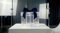 Elegant transparent gift box with navy blue ribbon bow on white pedestal in modern studio lighting setup for luxury product photography.