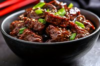 Glazed beef chunks in dark soy sauce garnished with green onions served in black ceramic bowl, close up view of Asian cuisine with rich brown sauce.