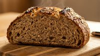 Freshly baked whole grain bread loaf with dense crumb structure, displayed on wooden cutting board for bakery, food photography, culinary blogs and restaurant menus.