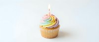 Vanilla cupcake with rainbow swirl frosting and lit candle on white background, suitable for birthday celebrations, bakery marketing, and festive event designs.