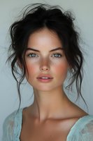 Young woman with messy dark hair updo, bright blue eyes, natural freckles and rosy cheeks wearing light turquoise dress against neutral background, beauty portrait.