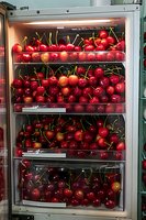 Fresh ripe red cherries on refrigerator shelves at grocery store, bright juicy fruits stacked in rows, food market produce display with natural lighting.