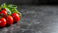 Fresh red cherry tomatoes on vine with water drops and green leaves against dark stone background, copy space for menu or recipe design.