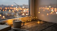 Cozy evening scene with coffee mug and fairy lights by window overlooking city bokeh lights. Warm atmosphere for relaxation and comfort concepts.
