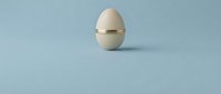 Cracked egg shell with golden band on minimalist blue background for Easter design concepts and spring marketing materials.