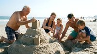 Multigenerational family building sandcastle together on beach, enjoying summer vacation and outdoor recreation with children and elderly grandfather.