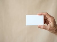 Male hand holding blank white business card against neutral beige background, suitable for branding, corporate identity, and marketing mockup designs.