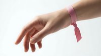 Female hand with pink ribbon tied around wrist symbolizing breast cancer awareness and support on white background for healthcare campaigns.